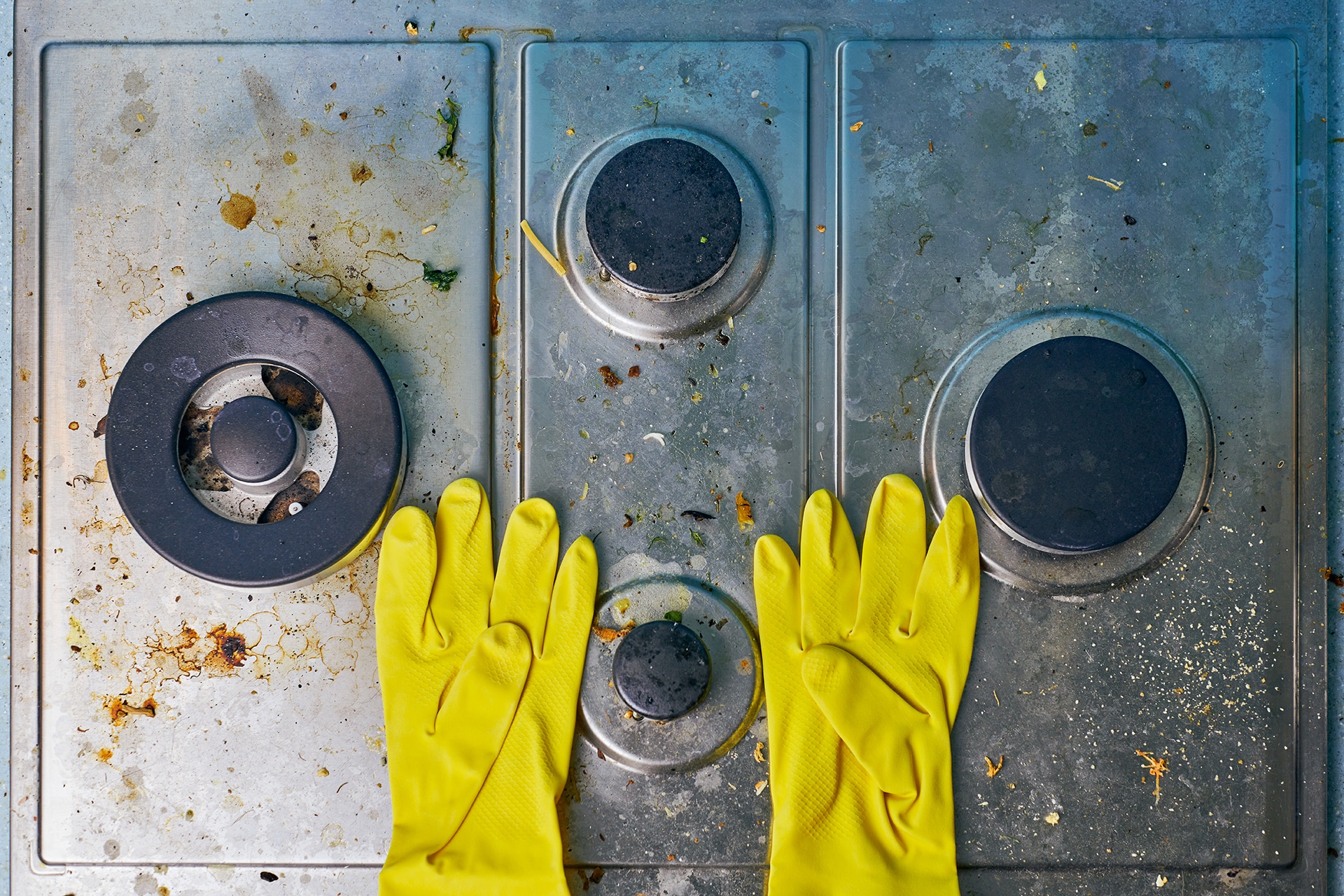 Dirty stove top with yellow cleaning gloves.