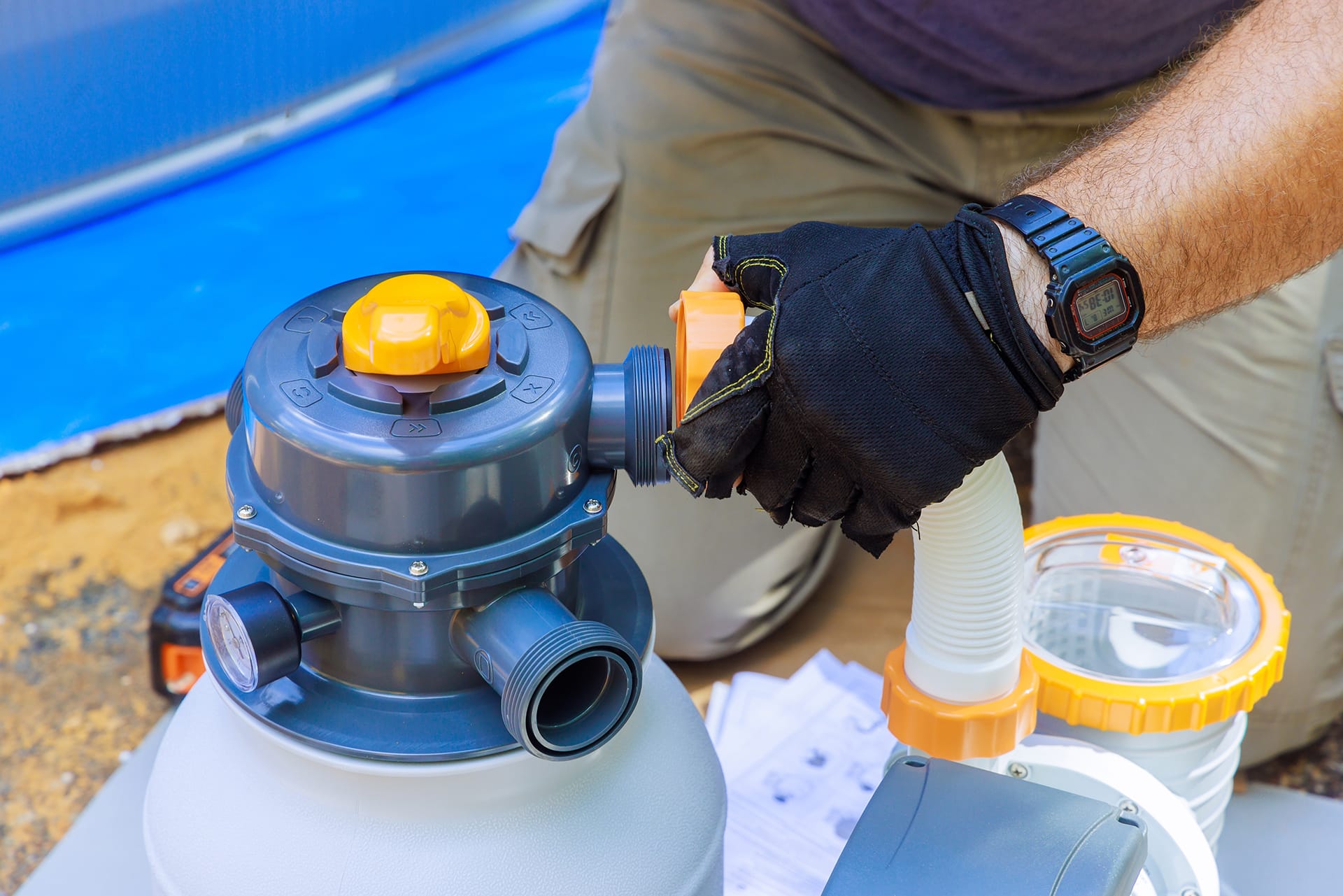 Person assembling pool filter equipment outdoors.