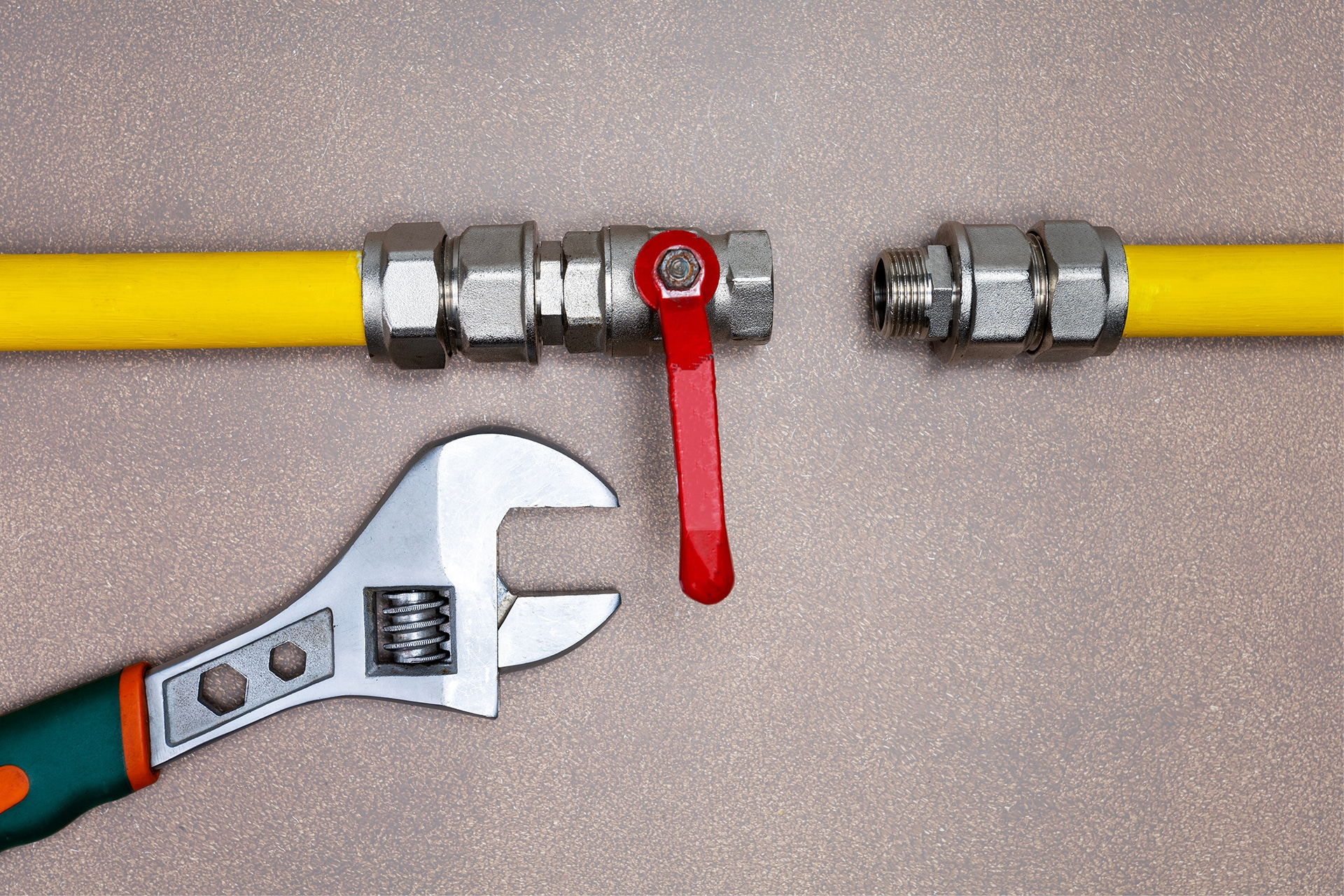 Adjustable wrench near gas valve on yellow pipeline.