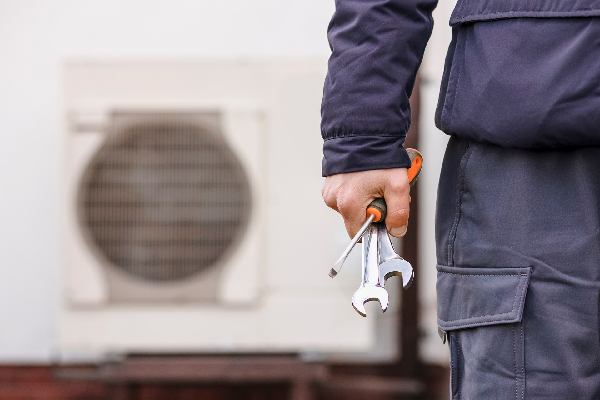 Technician with tools near outdoor air conditioner unit.