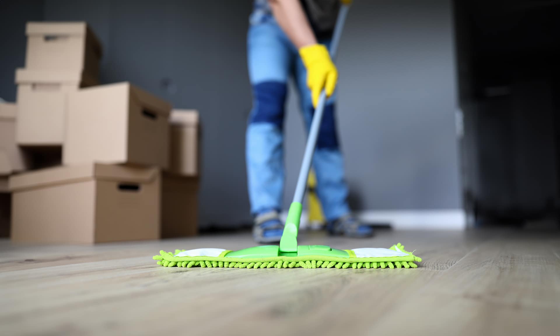Person mopping wood floor near moving boxes.