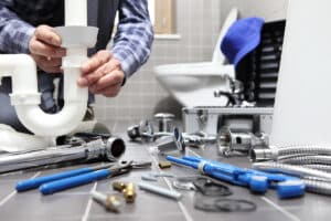 Plumber fixing sink with tools and pipes nearby.