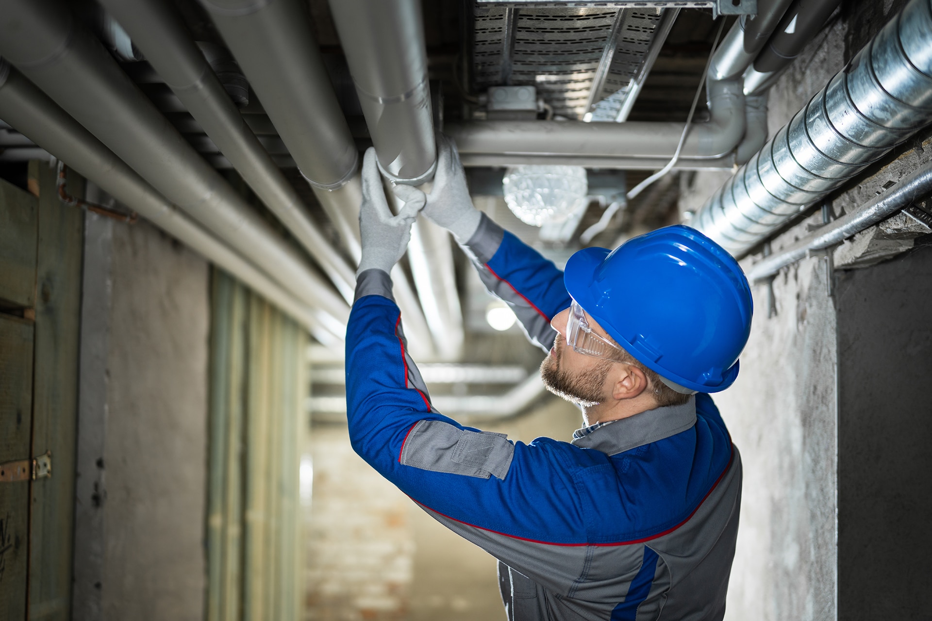 Worker inspecting industrial pipes with hard hat.