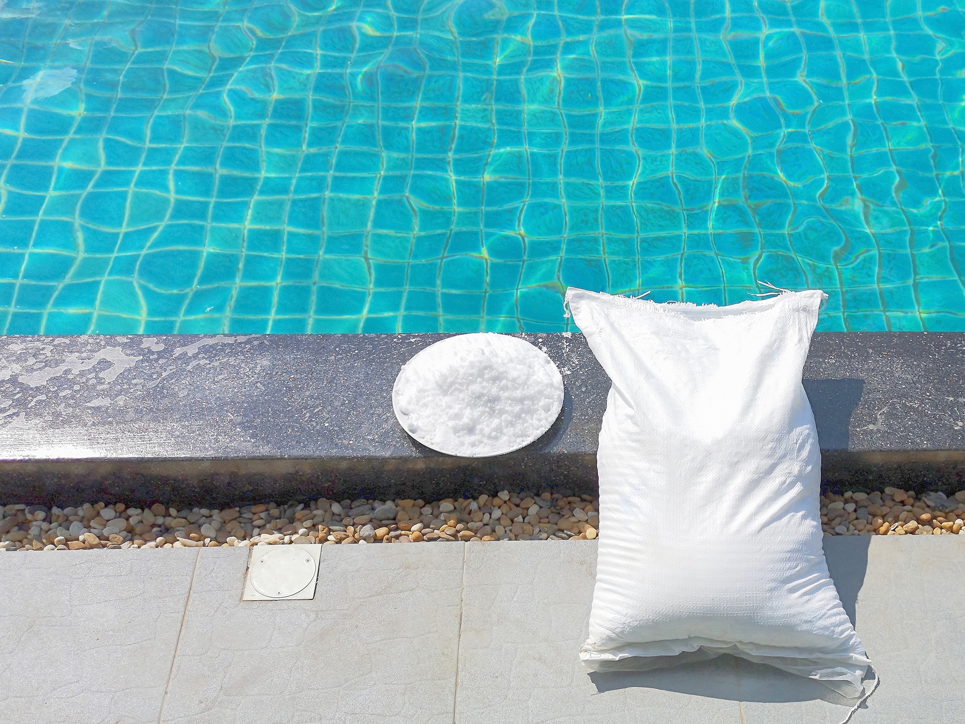 White sack and poolside tiles by blue water.
