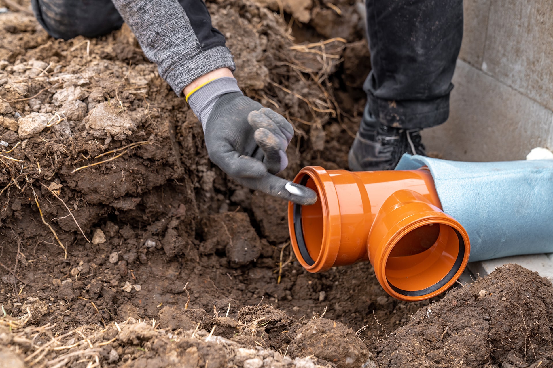 Person checking orange pipe connection in dirt.