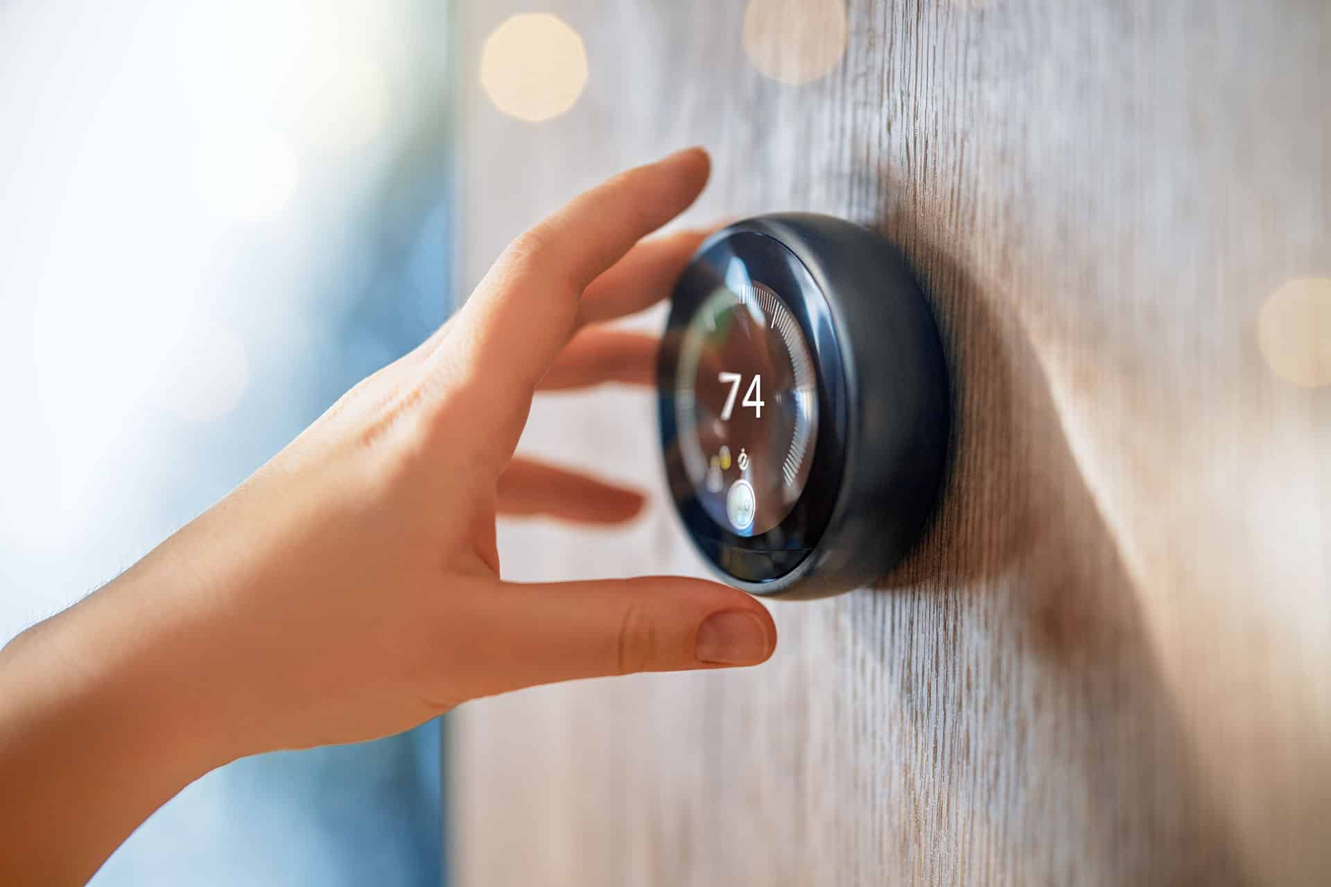 Hand adjusting smart thermostat to 74 degrees.