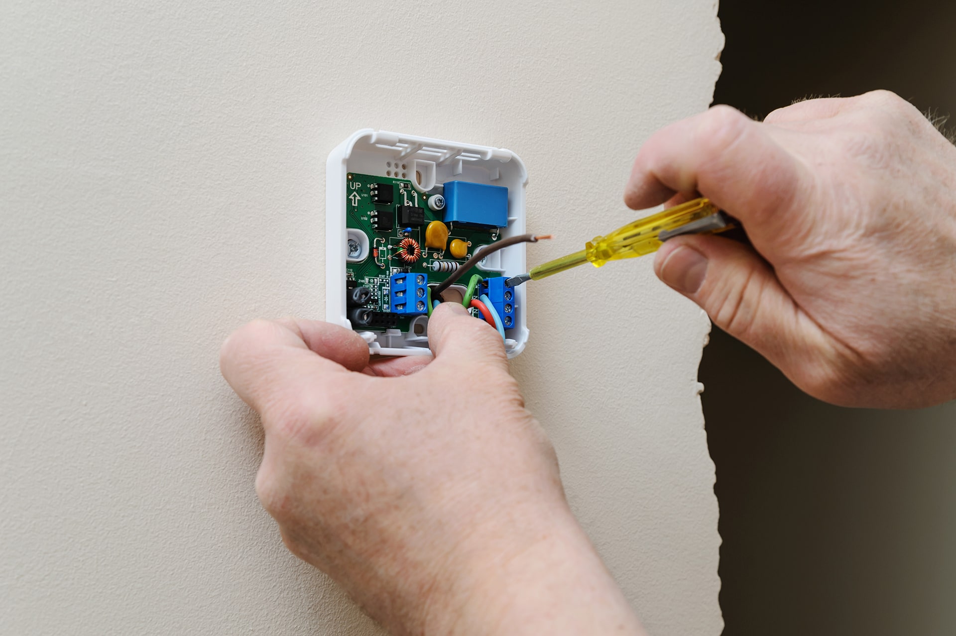 Person repairing thermostat wiring with screwdriver.
