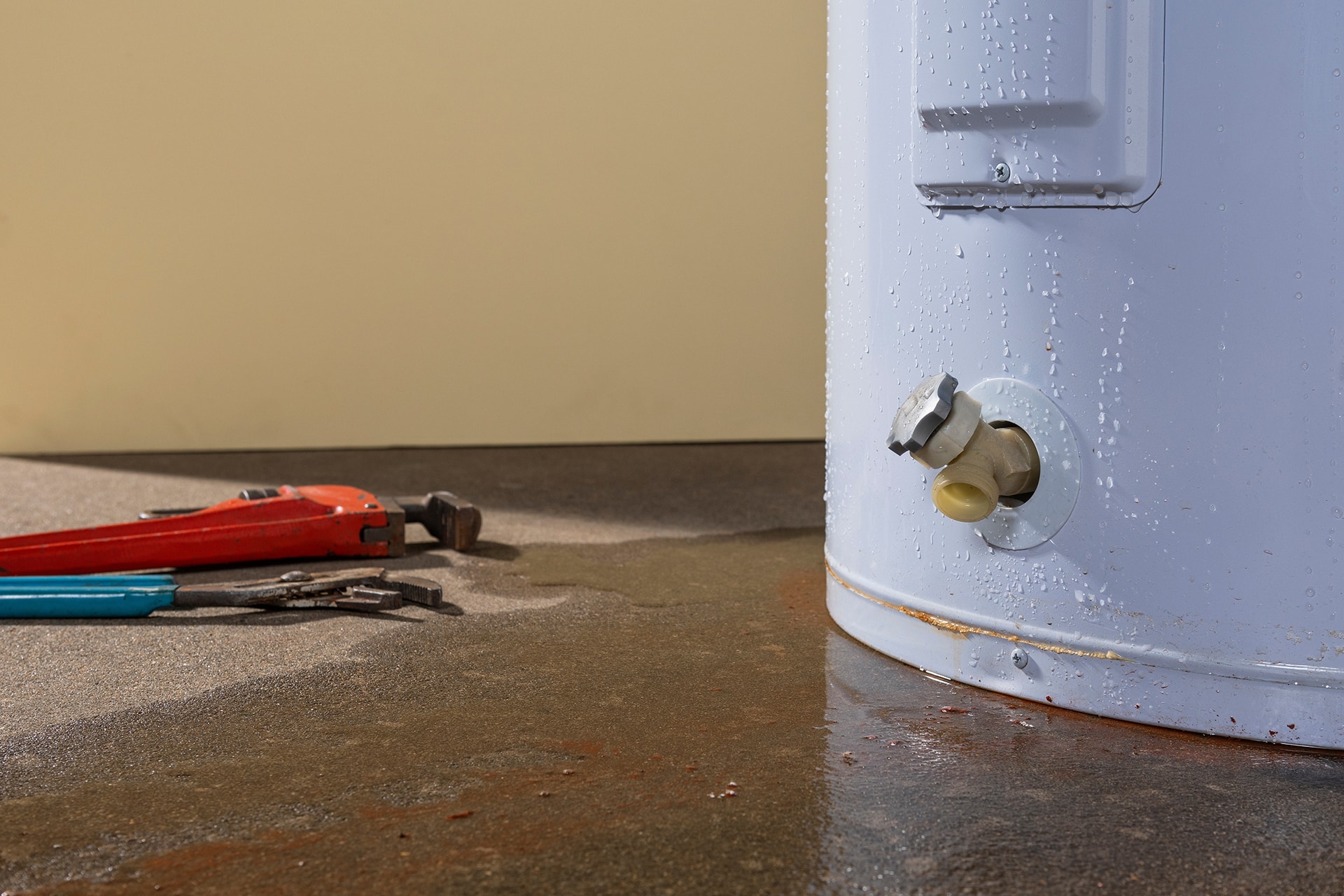 Leaky water heater with tools on wet floor.