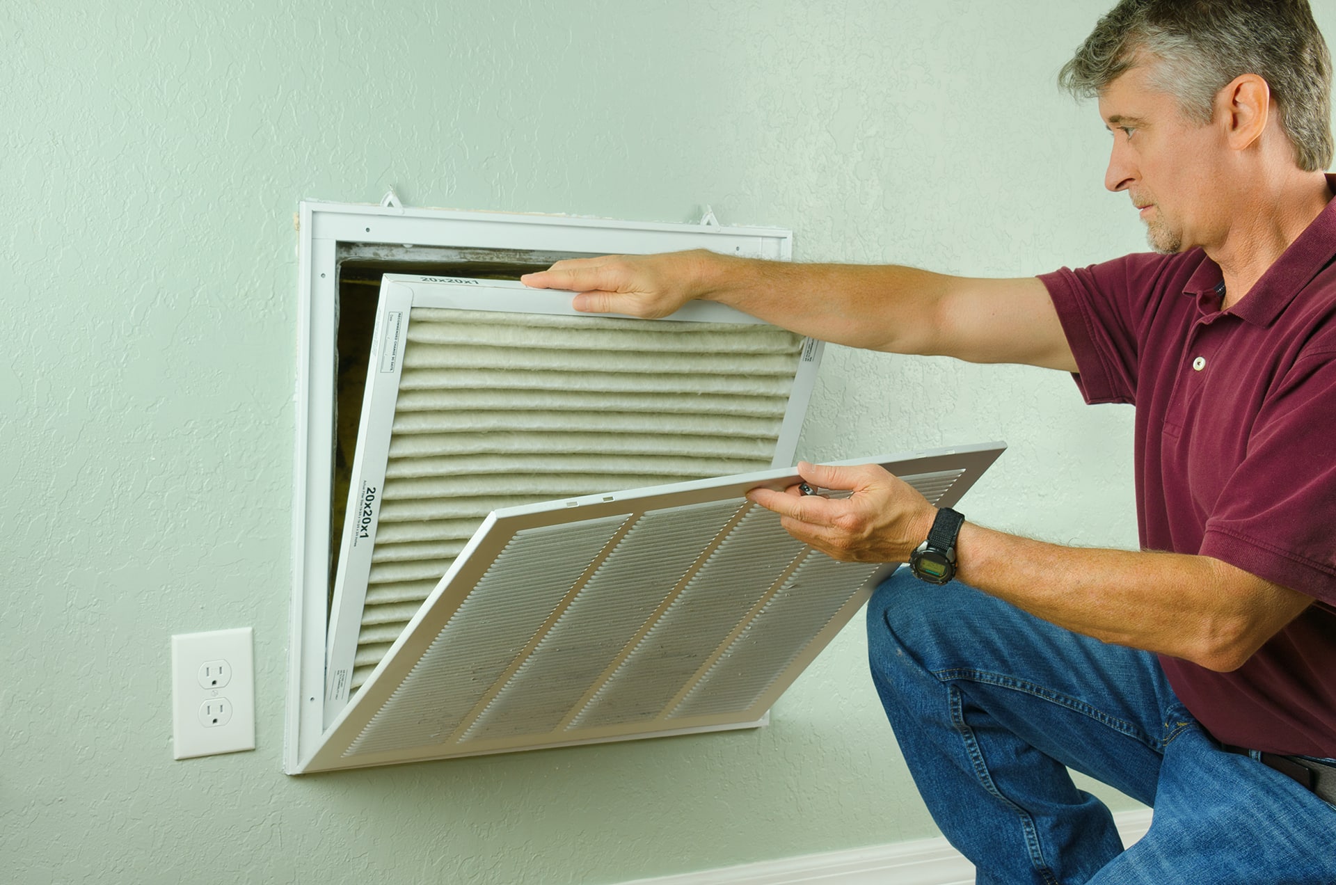 Man replacing air filter in wall vent.