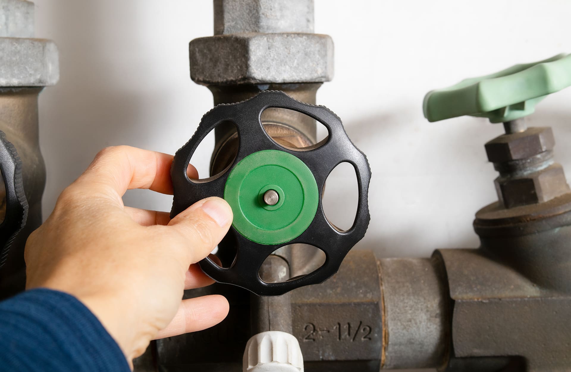 Person adjusting green valve on industrial pipe