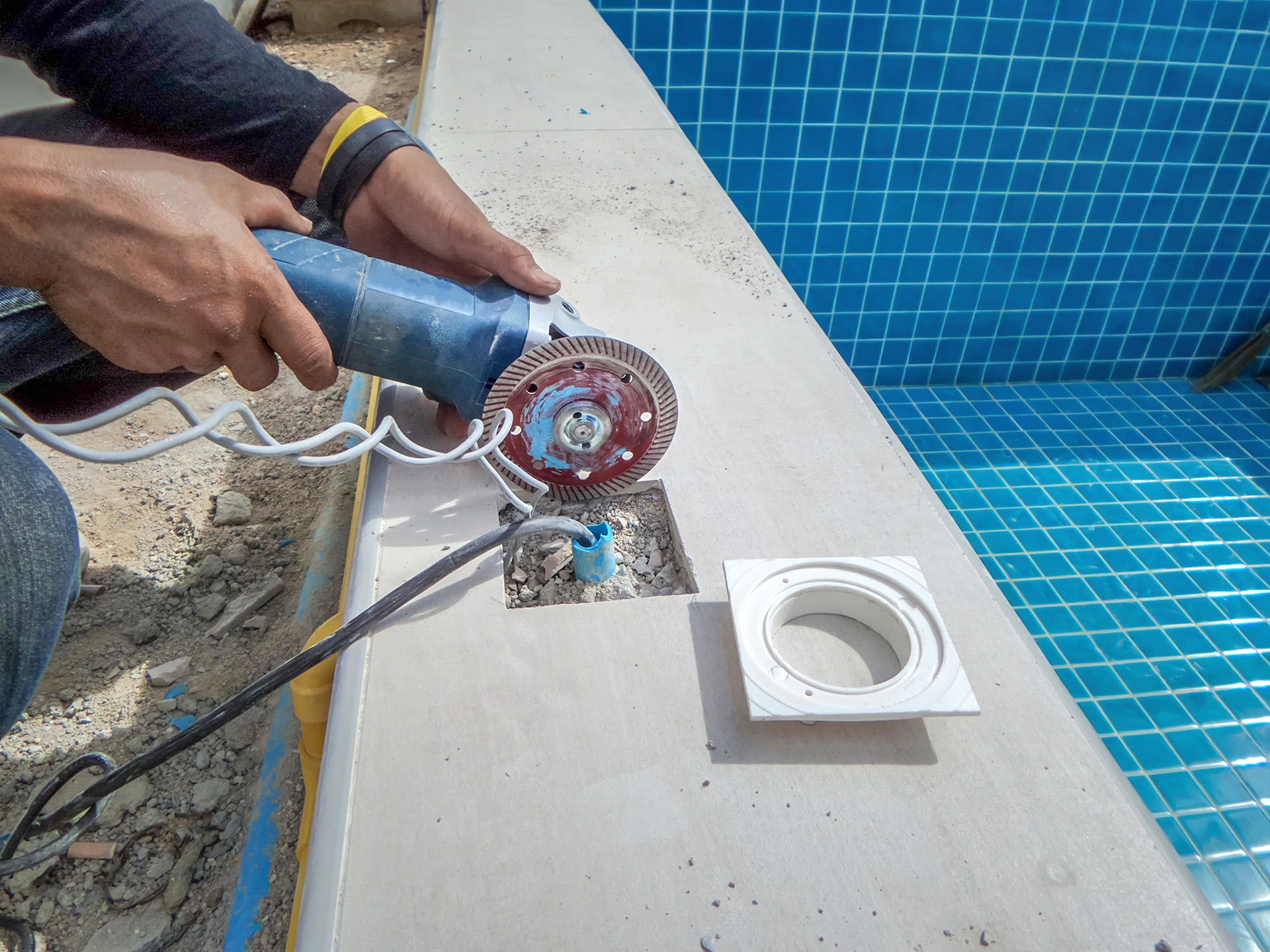 Worker cutting poolside tiles with angle grinder.