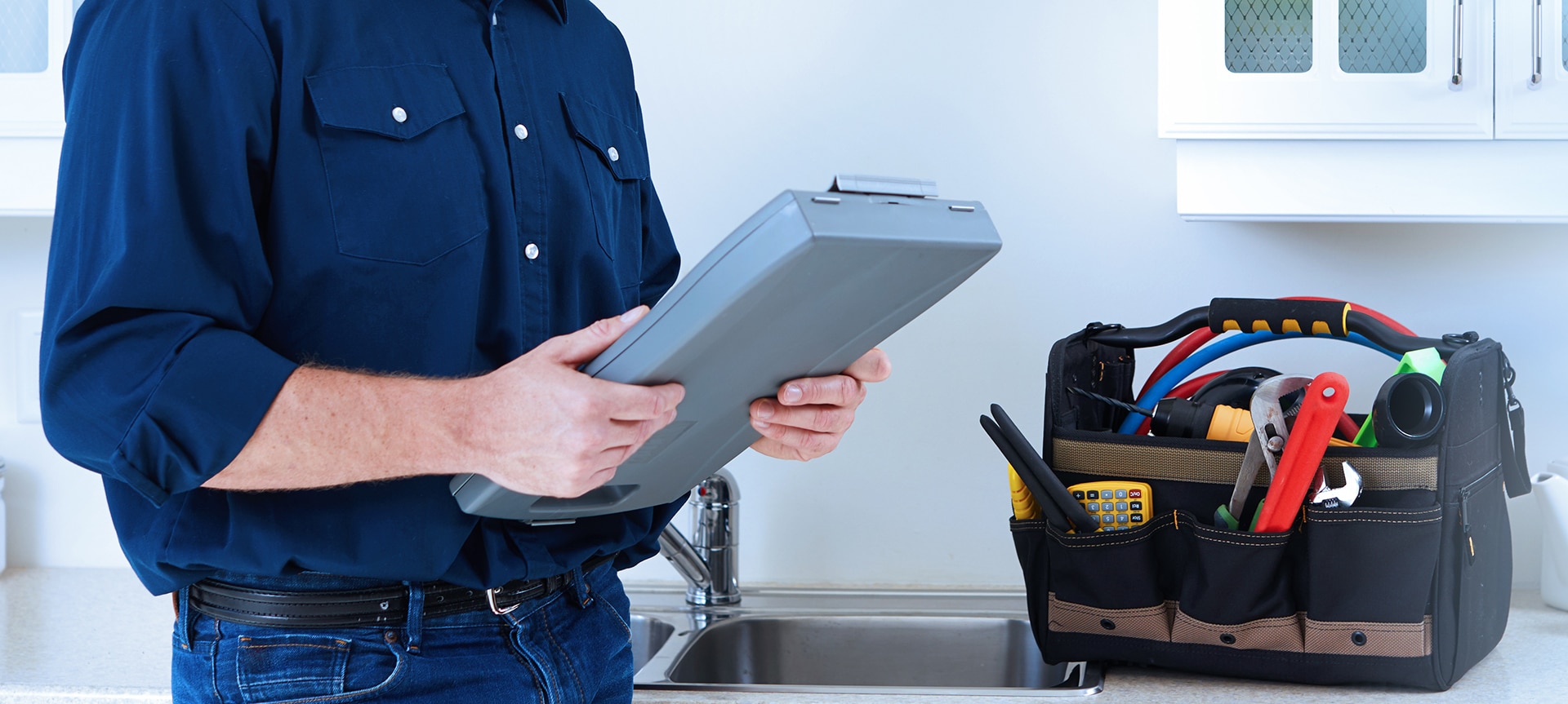 Man holding clipboard next to tool bag on countertop.