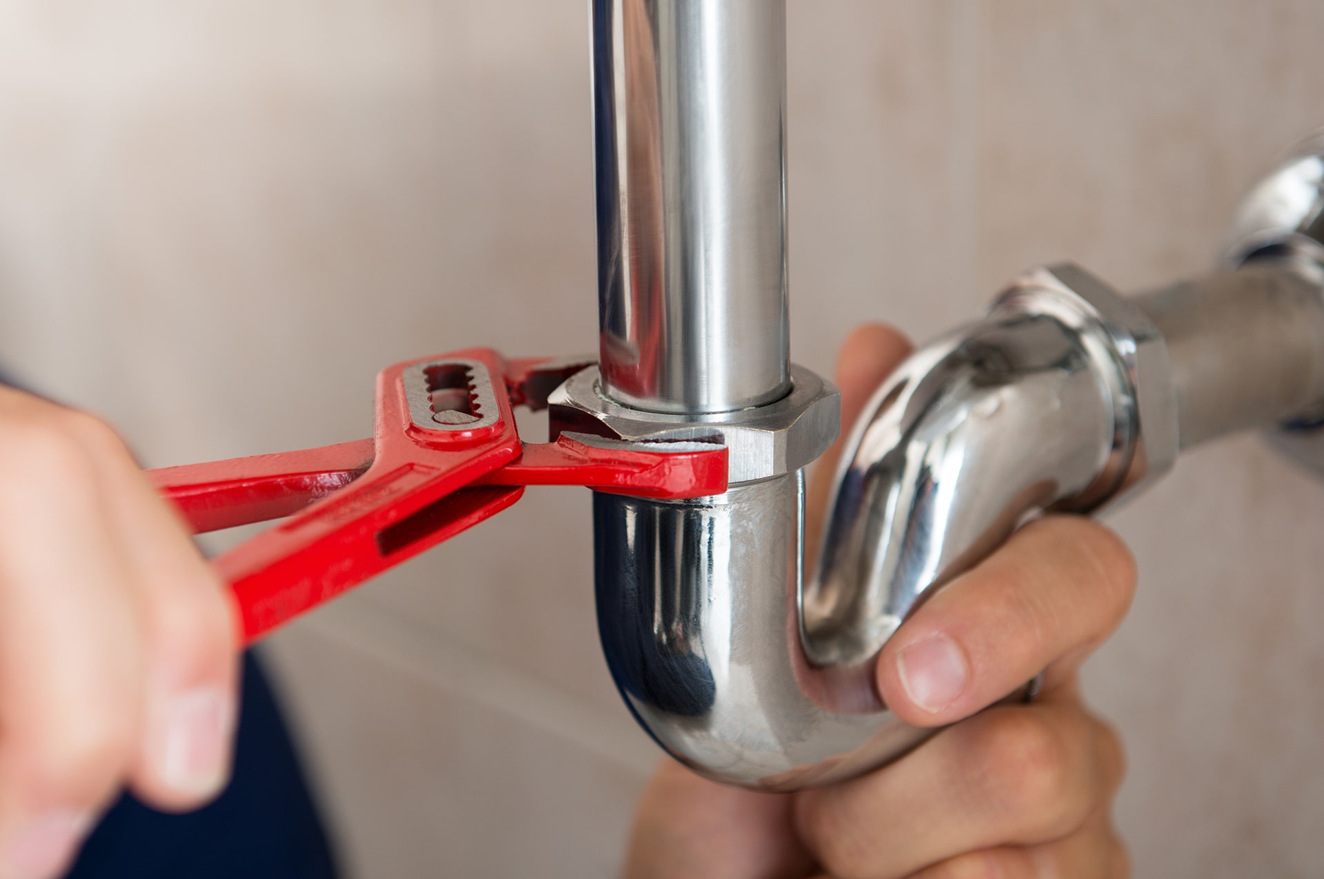 Plumber tightening pipe with wrench, close-up view.