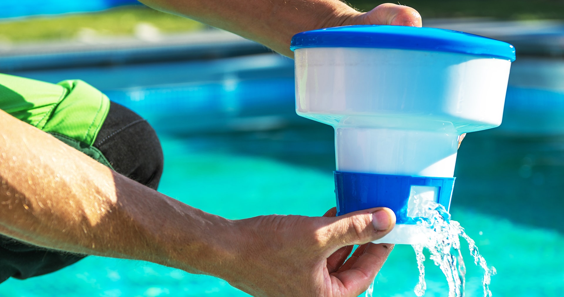 Person holding pool chemical dispenser over water.
