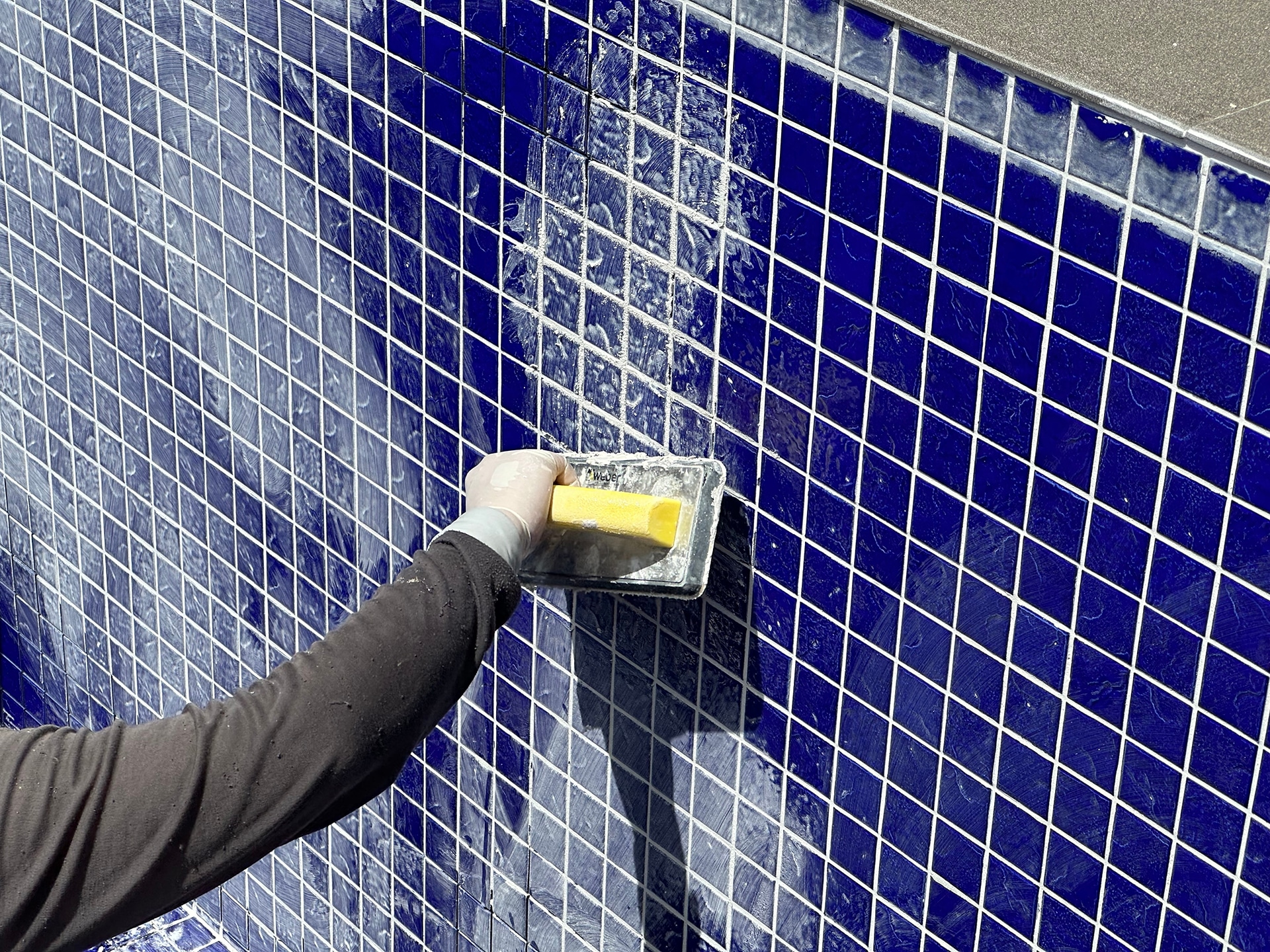 Applying grout to blue tiled wall
