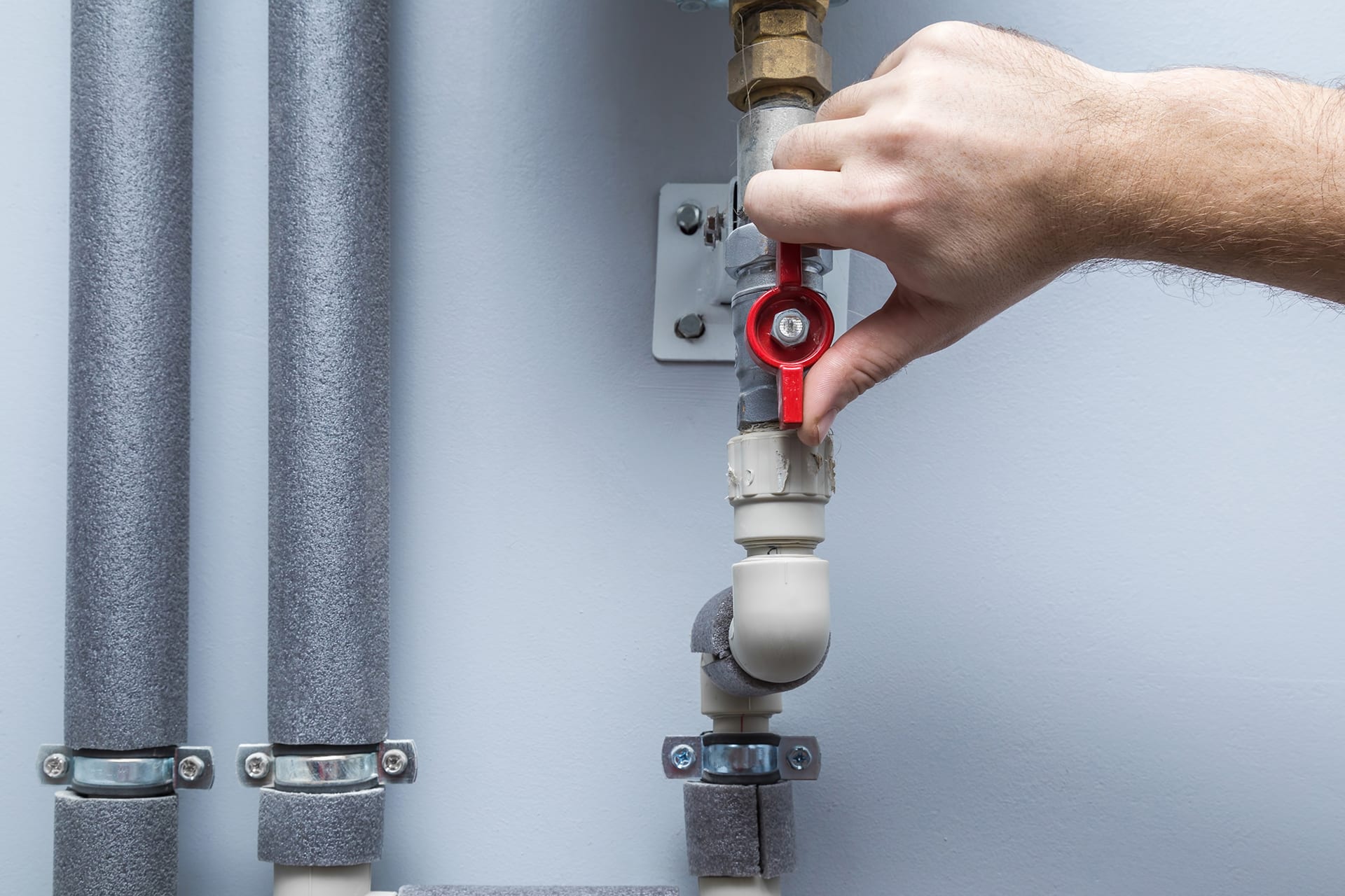 Hand turning red valve on insulated pipes.