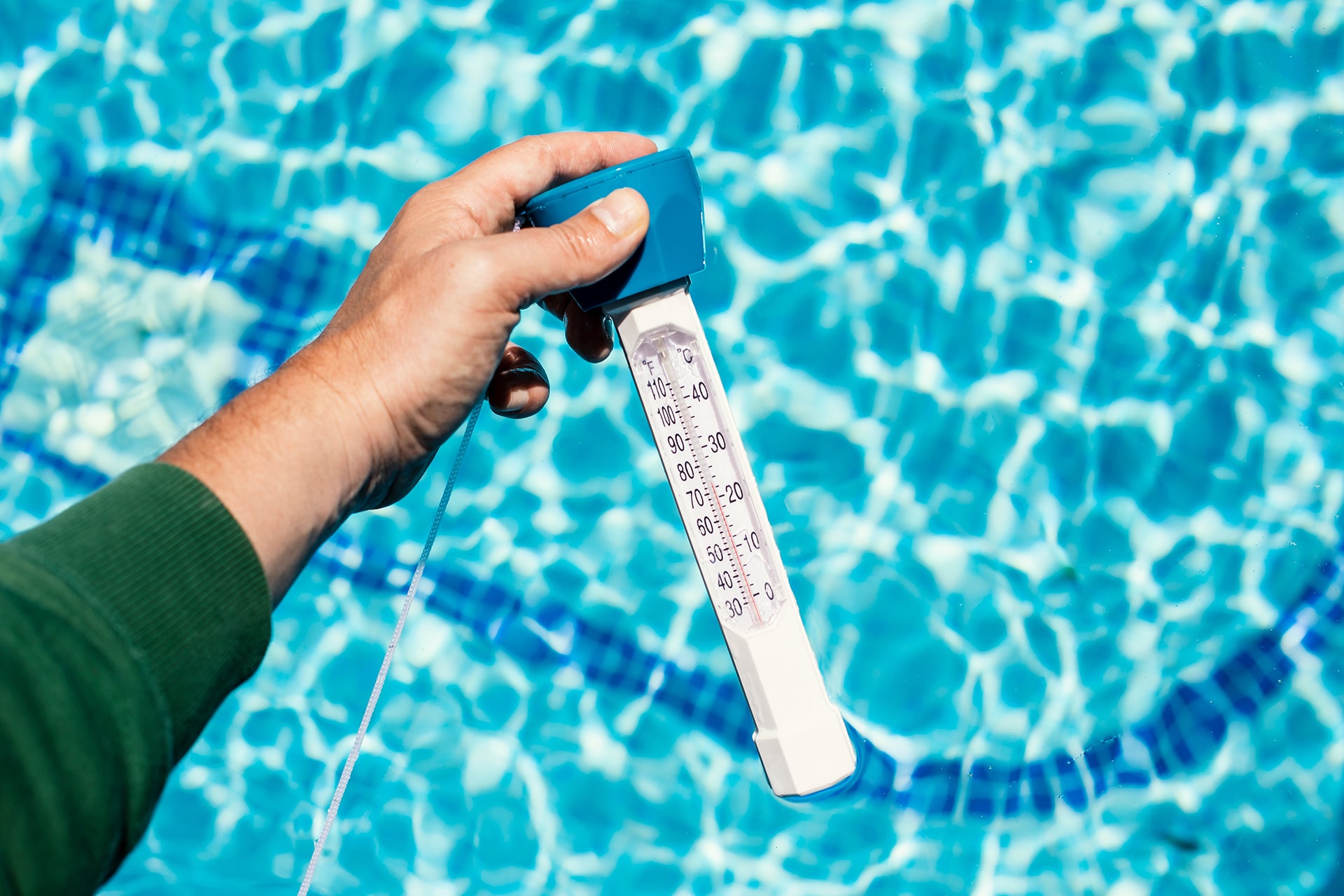 Hand holding pool thermometer over water